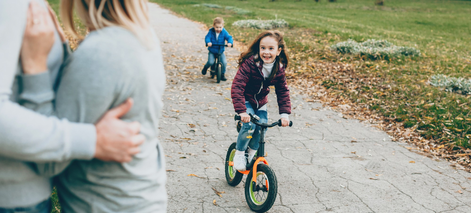 Jolie fille avec petit frère à vélo dans le parc pendant que les parents les regardent